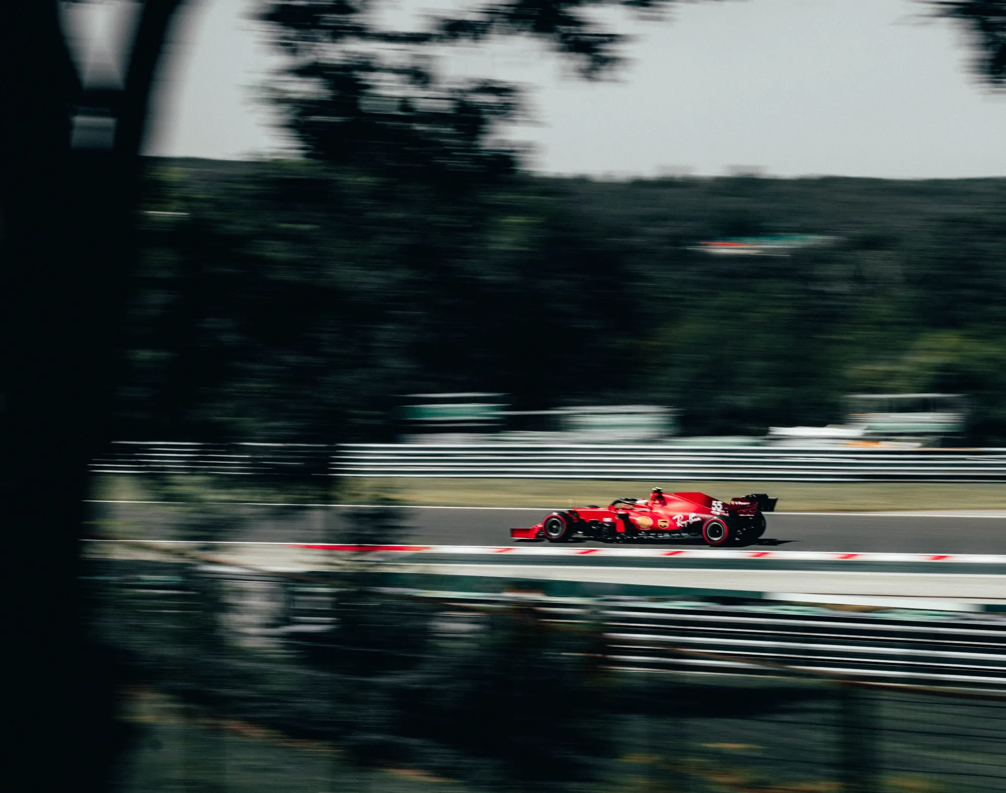 A red Formula 1 car seen at speed through the trees lining the circuit