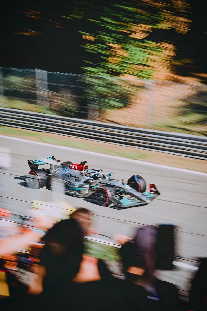 A Formula 1 car at speed past the grandstands, the crowd blurred in the foreground